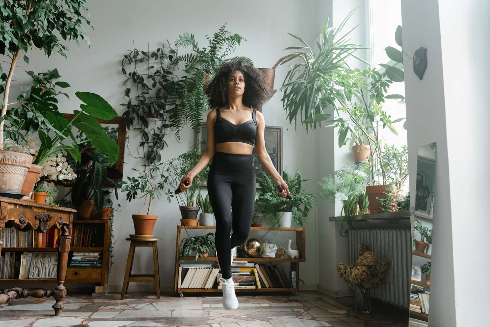 A person skipping rope in the open floor space of a plant-filled apartment room